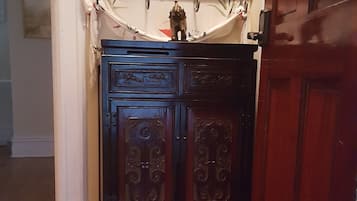 Una puerta de madera con manija de latón, un mueble azul oscuro con detalles ornamentales y un felpudo con la palabra "NAMASTE".