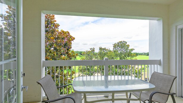 Ein Balkon mit Glastisch und zwei Stühlen mit Blick auf eine grüne Landschaft.