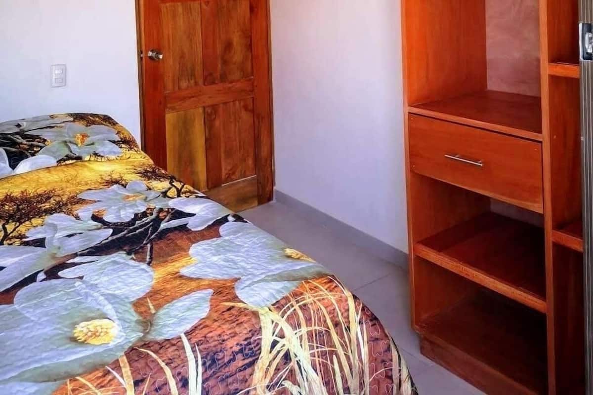 A bedroom with a wooden door, a bed with a floral bedspread, and a wooden wardrobe with hangers.