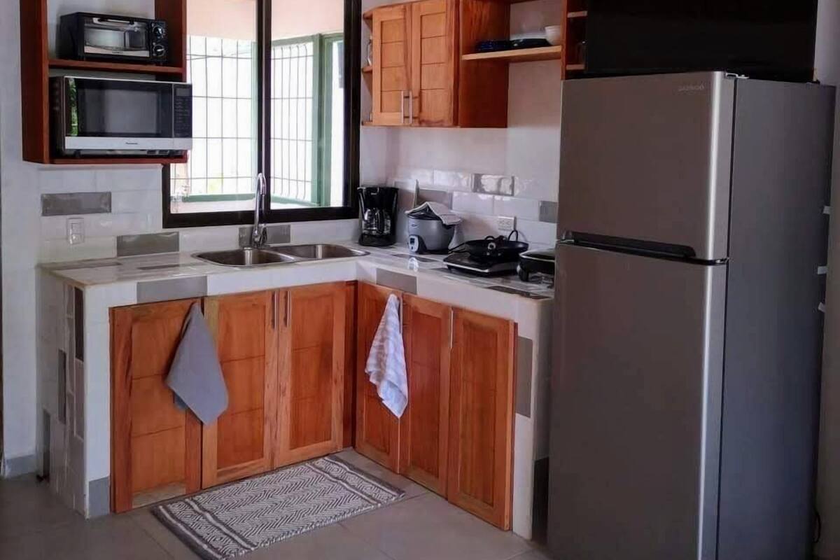 A compact kitchen with wooden cabinets, a stainless steel refrigerator, and a microwave.