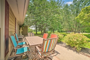 Relax in the serene outdoor patio surrounded by lush greenery, featuring a wooden table and six comfortable chairs.