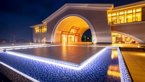 Un bâtiment moderne doté d’une grande entrée en arc de cercle et d’un espace piscine carrelé.