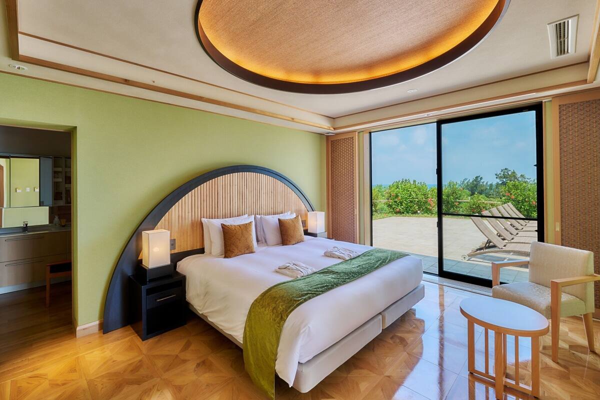 Ein Hotelzimmer mit Bett, Schreibtisch, Stuhl, großem Fenster und Deckenleuchte.