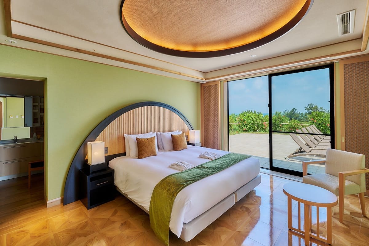 Une chambre d’hôtel équipée d’un lit, d’un bureau, d’une chaise, d’une grande fenêtre et d’un luminaire au plafond.