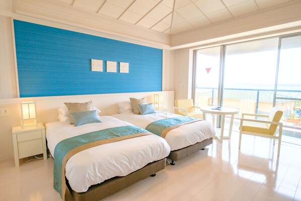 A hotel room with two beds, a balcony with a view, and a small table with a chair. - Seawood Hotel (Miyakojima)