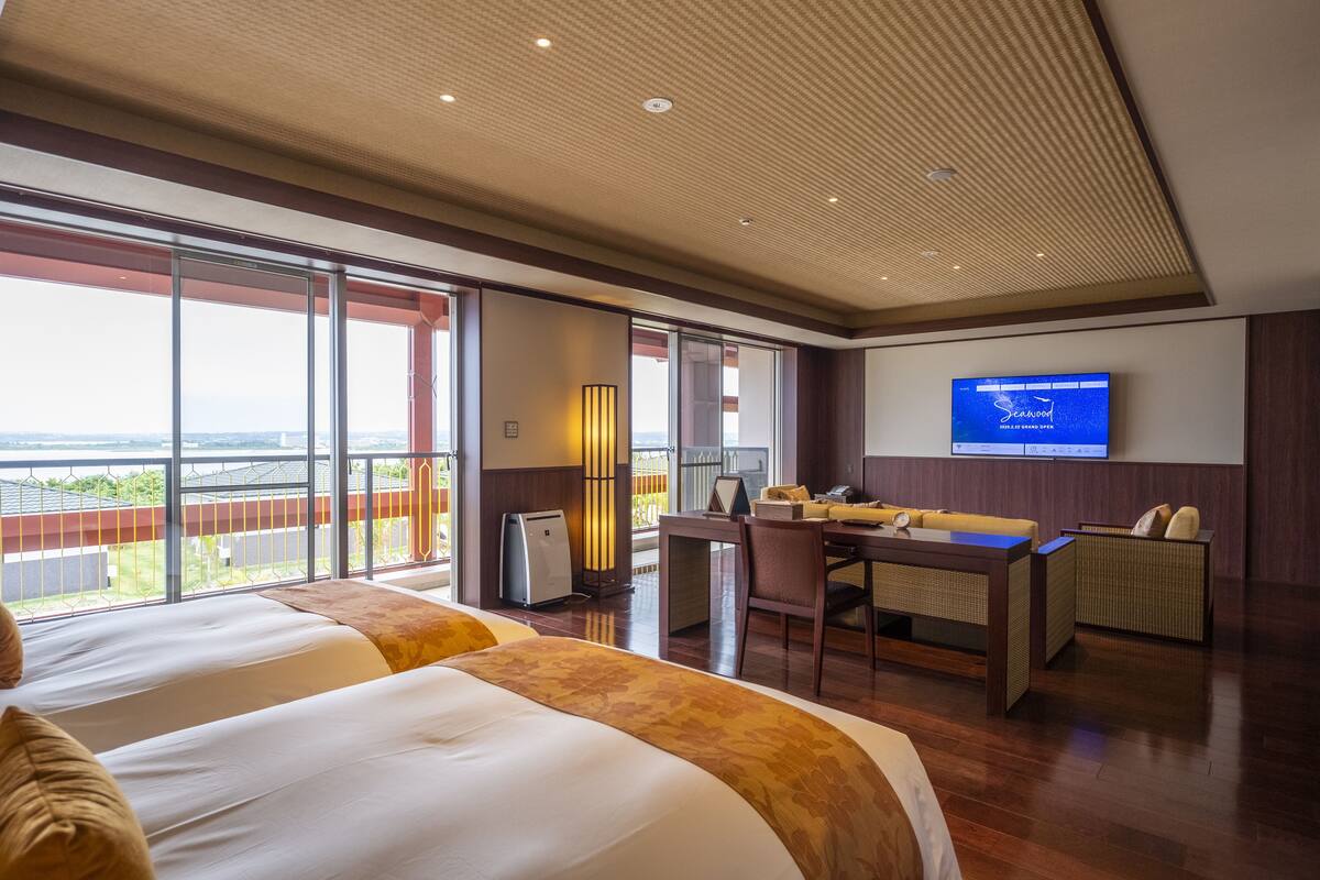 Ein Hotelzimmer mit einem großen Bett, einem Schreibtisch, einem Stuhl, einem Fernseher und einem Balkon mit Blick.