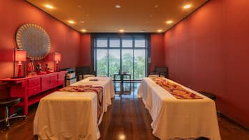 Traditional hotel room with two single beds, a central table, and a red desk with a lamp.