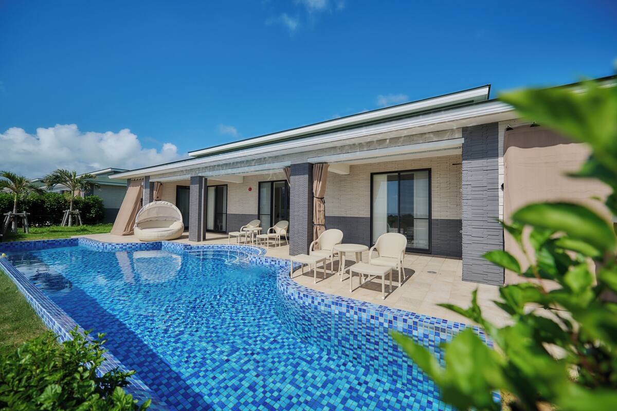 Ein modernes Haus mit Schwimmbad, Sitzgelegenheiten im Freien und einer überdachten Terrasse.
