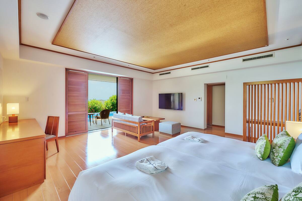 Ein Hotelzimmer mit einem großen Bett, einem Schreibtisch, einem Sessel, einem Fernseher und einer Schiebetür zum Balkon.