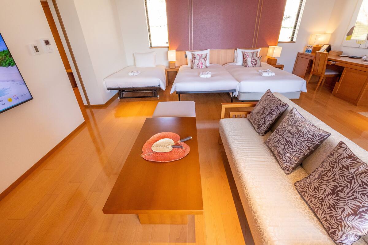 Ein Hotelzimmer mit zwei Betten, einem Schlafsofa, einem Holztisch und einem Fernseher an der Wand.