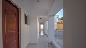 Un corridoio con una porta rossa, pareti bianche e pavimento piastrellato, che conduce a una porta alla fine.