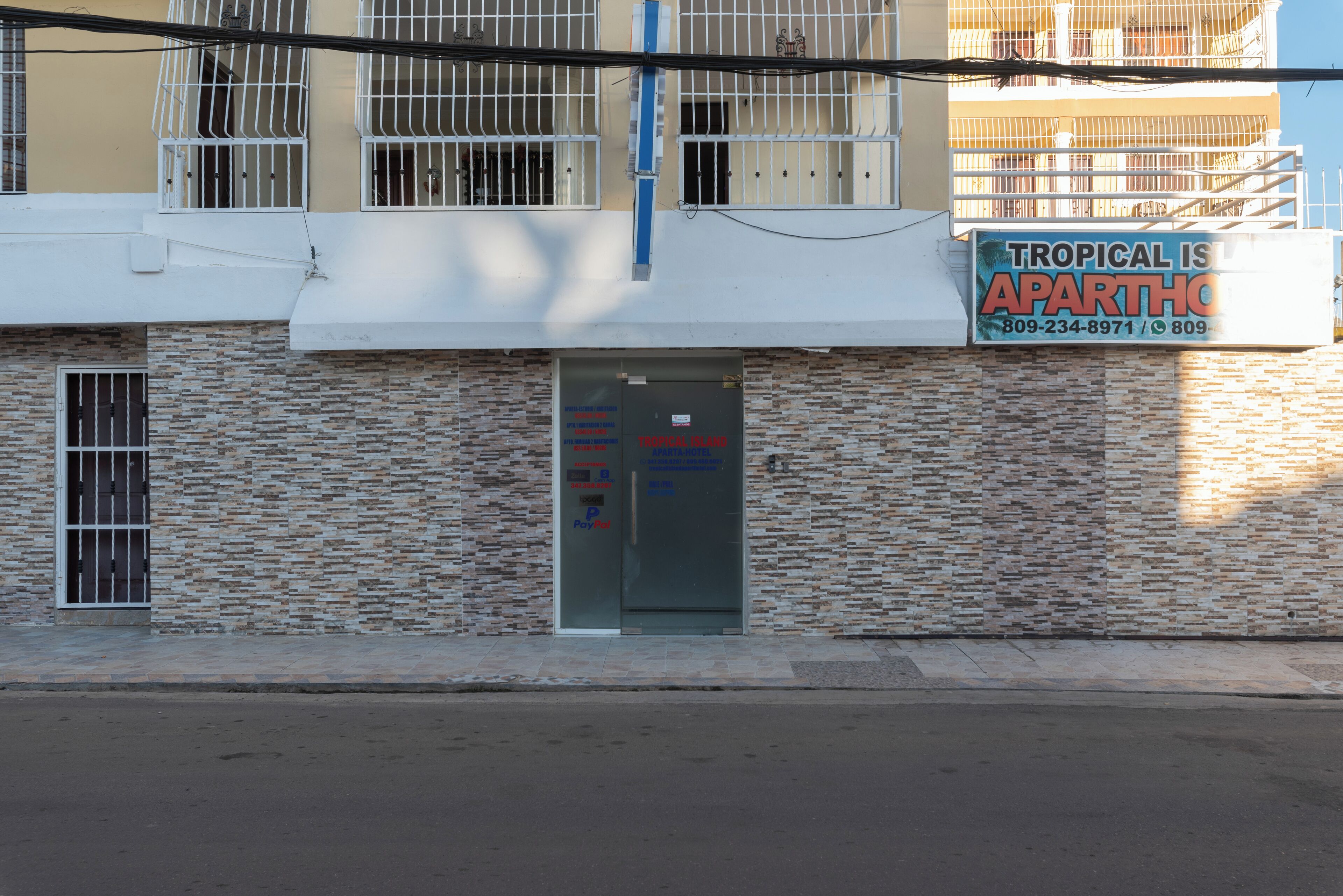 Un immeuble à la façade en pierre, avec une entrée dotée d’une porte en verre et une enseigne publicitaire indiquant : « Tropical is Aparthos ».