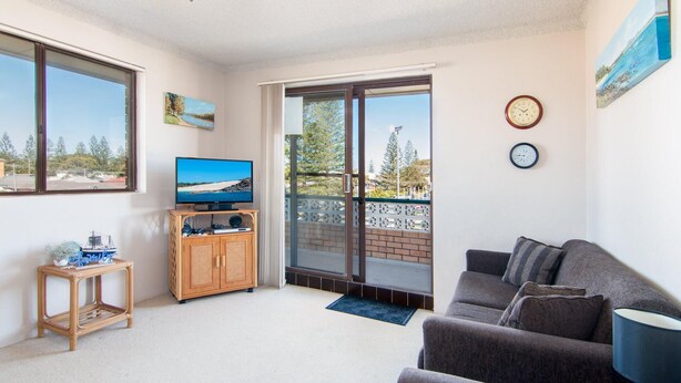 A living room with a television, a couch, and a view of a beach through a sliding door. - Seabreeze 4 - Opposite Tuncurry Bowling Club! (Tuncurry)