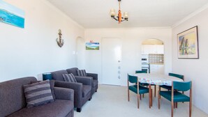 A compact living space with a sofa set, a dining table with chairs, a kitchen area, and a chandelier. - Seabreeze 4 - Opposite Tuncurry Bowling Club! (Tuncurry)
