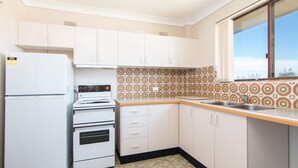 A compact kitchen with white cabinets, a white refrigerator, a stove, and a patterned backsplash. - Seabreeze 4 - Opposite Tuncurry Bowling Club! (Tuncurry)