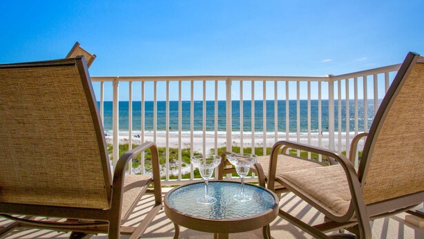 A balcony with two wicker chairs and a small table, overlooking a beach and the ocean. - Upgraded Beachfront Condo Close to Shops, and Restaurants - Pool, Hot Tub, Beach, and Private Balcony (Madeira Beach)