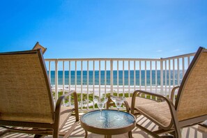 A balcony with two wicker chairs and a small table, overlooking a beach and the ocean. - Upgraded Beachfront Condo Close to Shops, and Restaurants- Pool, Hot Tub, Beach, and Private Balcony (Madeira Beach)