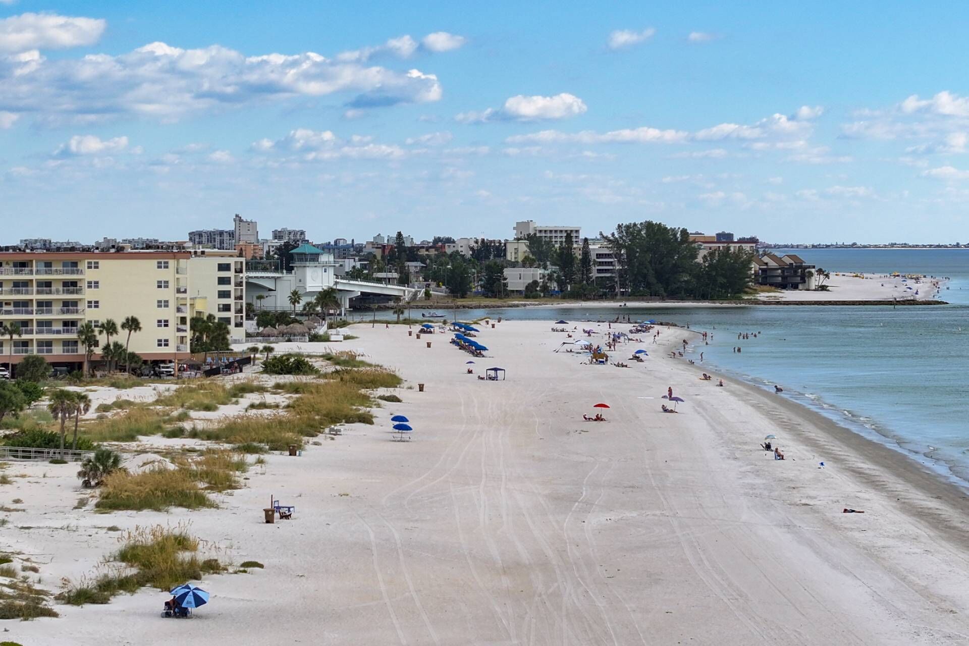 A beach with a clear sky, buildings in the background, and a sandy shore.