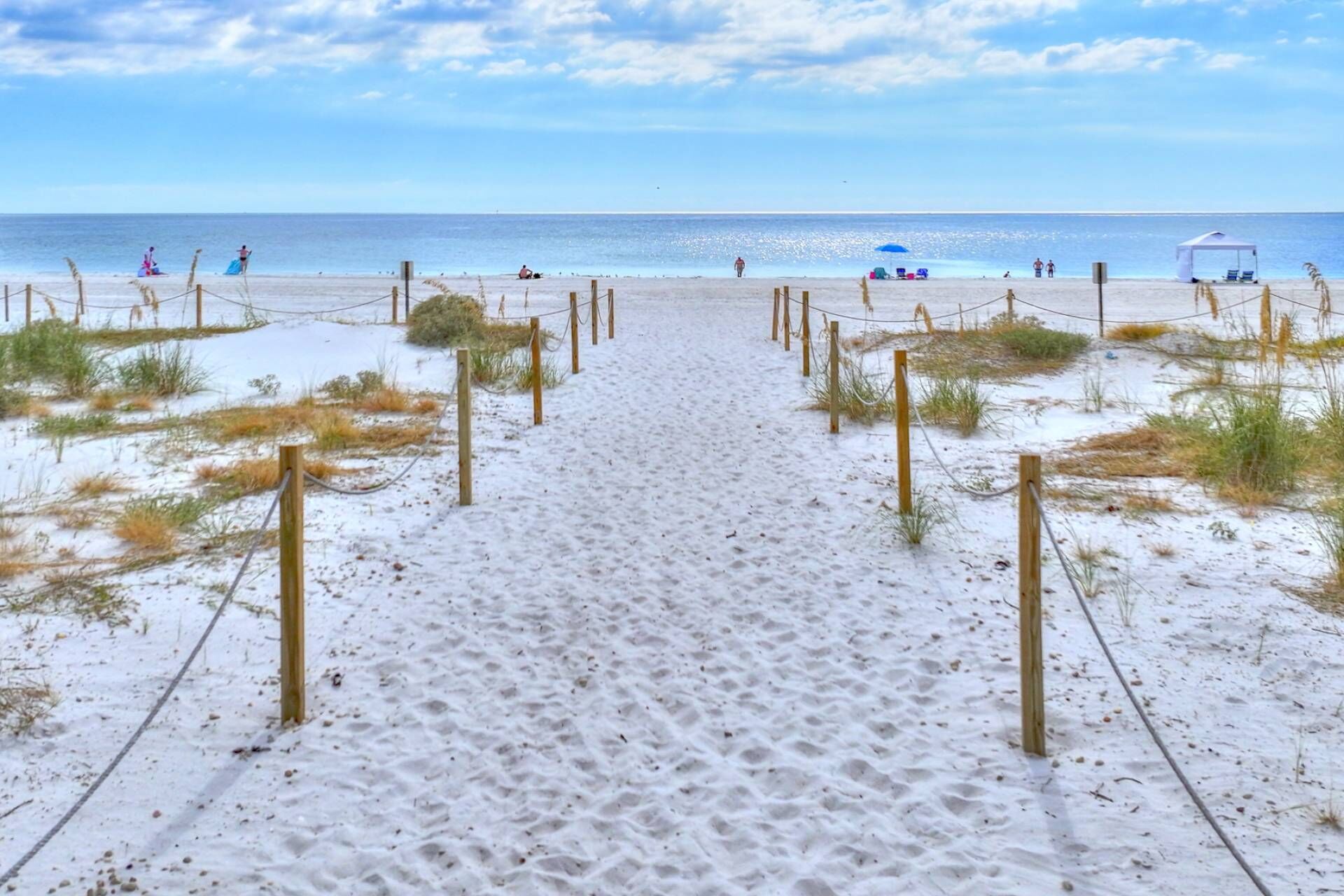 A sandy beach path leading to the ocean with a clear sky.