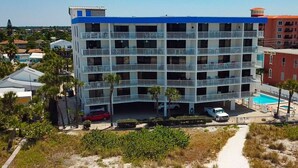 A multi-story hotel with a blue roof and white balconies, surrounded by greenery and a sandy path. - Upgraded Beachfront Condo Close to Shops, and Restaurants - Pool, Hot Tub, Beach, and Private Balcony (Madeira Beach)
