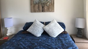 Een slaapkamer met een bed, twee kussens, een nachtkastje, een lamp en een kunstwerk aan de muur.