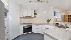 A modern kitchen with white cabinets, a built-in oven, a microwave, and a sink. - Kokomo Unit 1 Kings Beach QLD (CALOUNDRA)