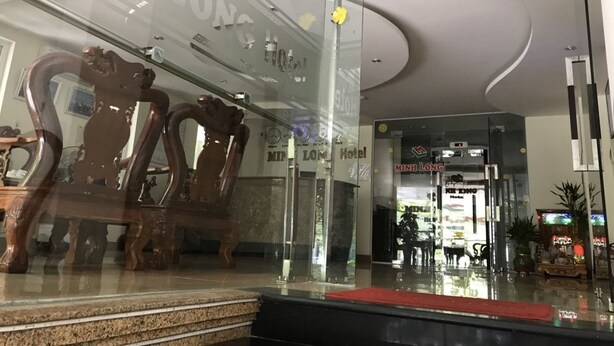 A hotel entrance with a glass facade, a wooden chair outside, and a sign reading "Min Long Hotel". - Minh Long Hotel (Da Nang)