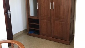 A wooden wardrobe with a mirrored door and two drawers, a wooden chair, and a tiled floor. - Minh Long Hotel (Da Nang)
