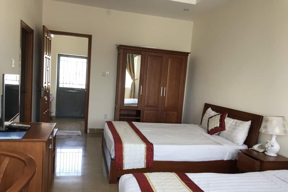 A hotel room with two beds, a wooden wardrobe, a desk with a computer, and a bedside table with a lamp.