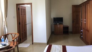 A hotel room with a bed, a wooden wardrobe, a television, and a desk with a chair and a bottle. - Minh Long Hotel (Da Nang)