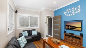 A modern living room with a black leather sofa, a wooden coffee table, and a wall-mounted TV displaying a sunset view. - Sandy Toes - park the car and walk everywhere! (Forster)