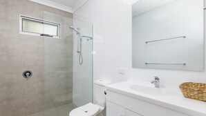 A modern bathroom with a glass-enclosed shower, a toilet, and a sink with a mirror above. - Sandy Toes - park the car and walk everywhere! (Forster)