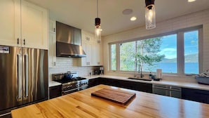 A modern kitchen with stainless steel appliances, a wooden island, and large windows offering a view of the outdoors. - Paradise Found, Modern Dream Home on Ashley Lake (Kila)