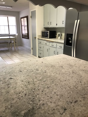 A kitchen with white cabinets, a granite countertop, a microwave, and a refrigerator.