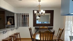 Un comedor con mesa y sillas de madera, una araña y un espejo grande sobre la mesa.