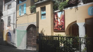 A building with a wooden door, a balcony with plants, and a mural on the wall.