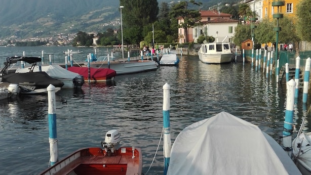 A calm lake with boats docked at the pier, surrounded by mountains and buildings.