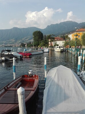 A calm lake with boats docked at the pier, surrounded by mountains and buildings.