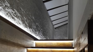 A wooden staircase with integrated lighting, leading to a room with a concrete wall and a sloped ceiling.