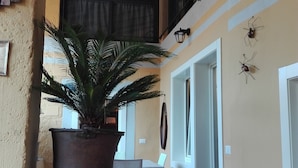 A covered outdoor area with a potted plant, a table, chairs, and a staircase leading to an upper level.