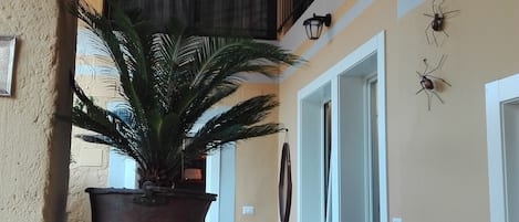 A covered outdoor area with a potted plant, a table, chairs, and a staircase leading to an upper level.