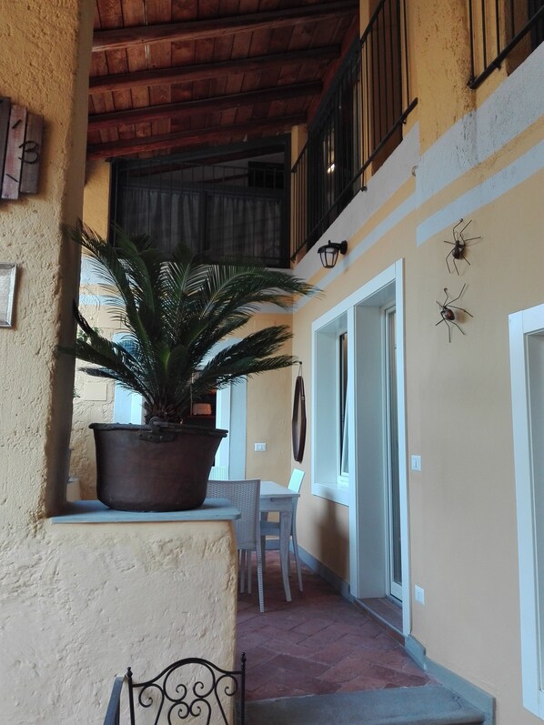A covered outdoor area with a potted plant, a table, chairs, and a staircase leading to an upper level.