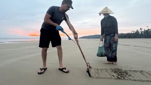 A man and a woman on a beach, one using a shovel and the other carrying a bag. - Co To Center Homestay (Co To)