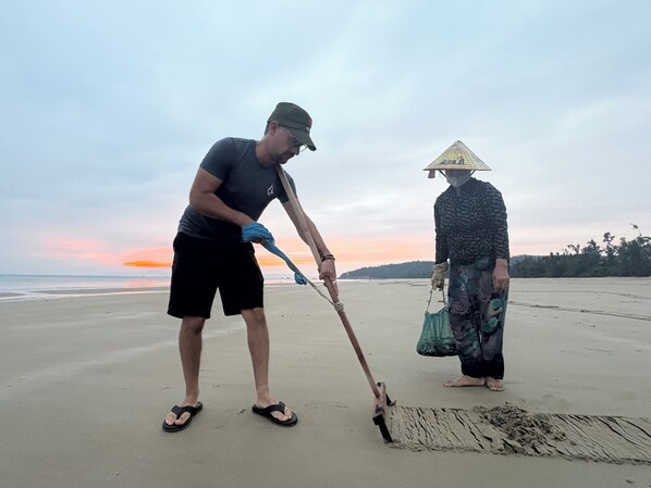 Un homme et une femme se trouvent sur une plage, l’un utilise une pelle et l’autre porte un sac.