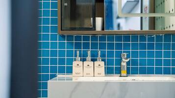 Une salle de bain avec un mur recouvert de carreaux bleus, un miroir et trois flacons de produits de toilette posés sur le lavabo.