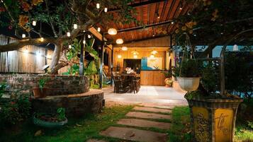 A covered outdoor area with a pathway leading to a building, surrounded by greenery and potted plants.