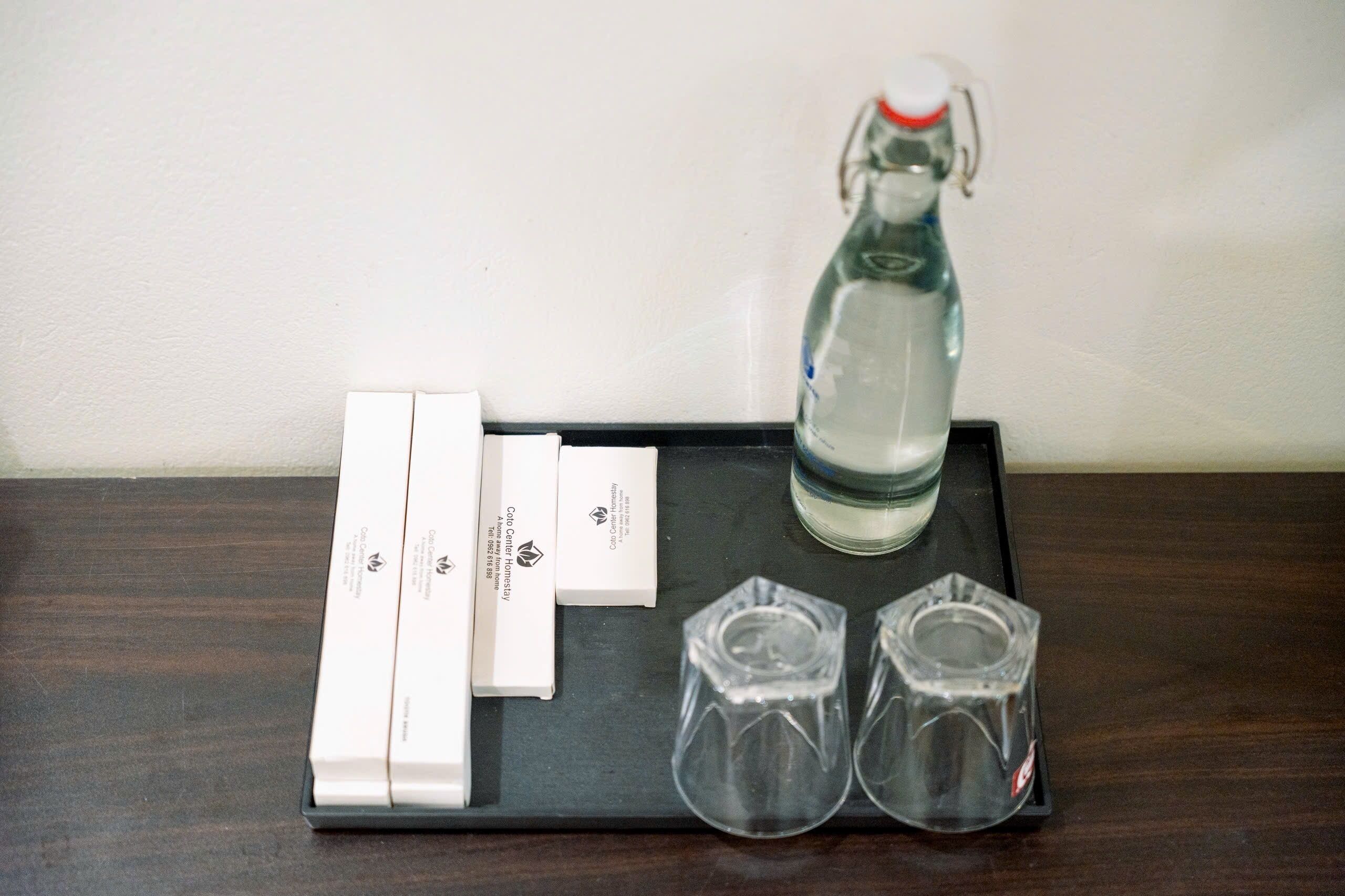 A tray with a water bottle, two glasses, and a set of white cards on a dark wooden surface.