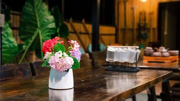 Ein Holztisch mit einer weißen Vase, die rosa und rote Blumen enthält, einer kleinen weißen Tischdecke und einer Platte mit Gebäck.