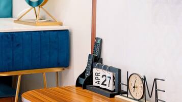 A room with a wooden desk, a blue chair, a wall-mounted TV, a clock, and a calendar.