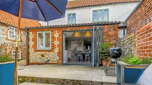Eine Terrassenfläche mit Holzdeck, Grill und Esstisch mit Stühlen.